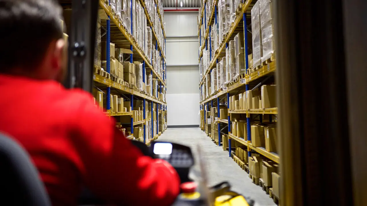 An employee drives a forklift truck through the rows of shelves in the warehouse