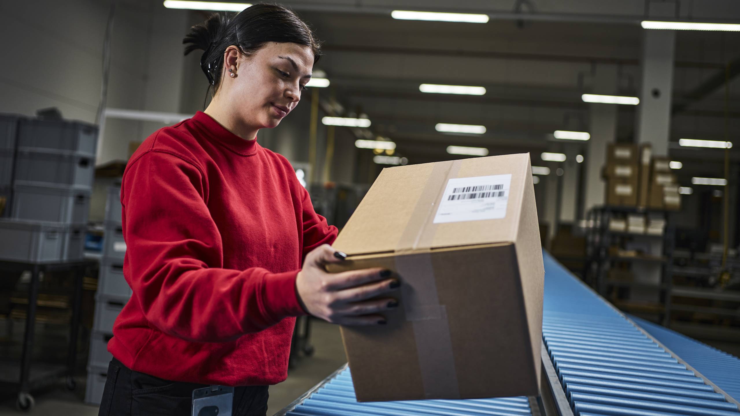 Eine Mitarbeiterin im Fulfillment legt eine fertig gepackte Bestellung auf ein Laufband, welches das Paket zur Warenausgabe befördert