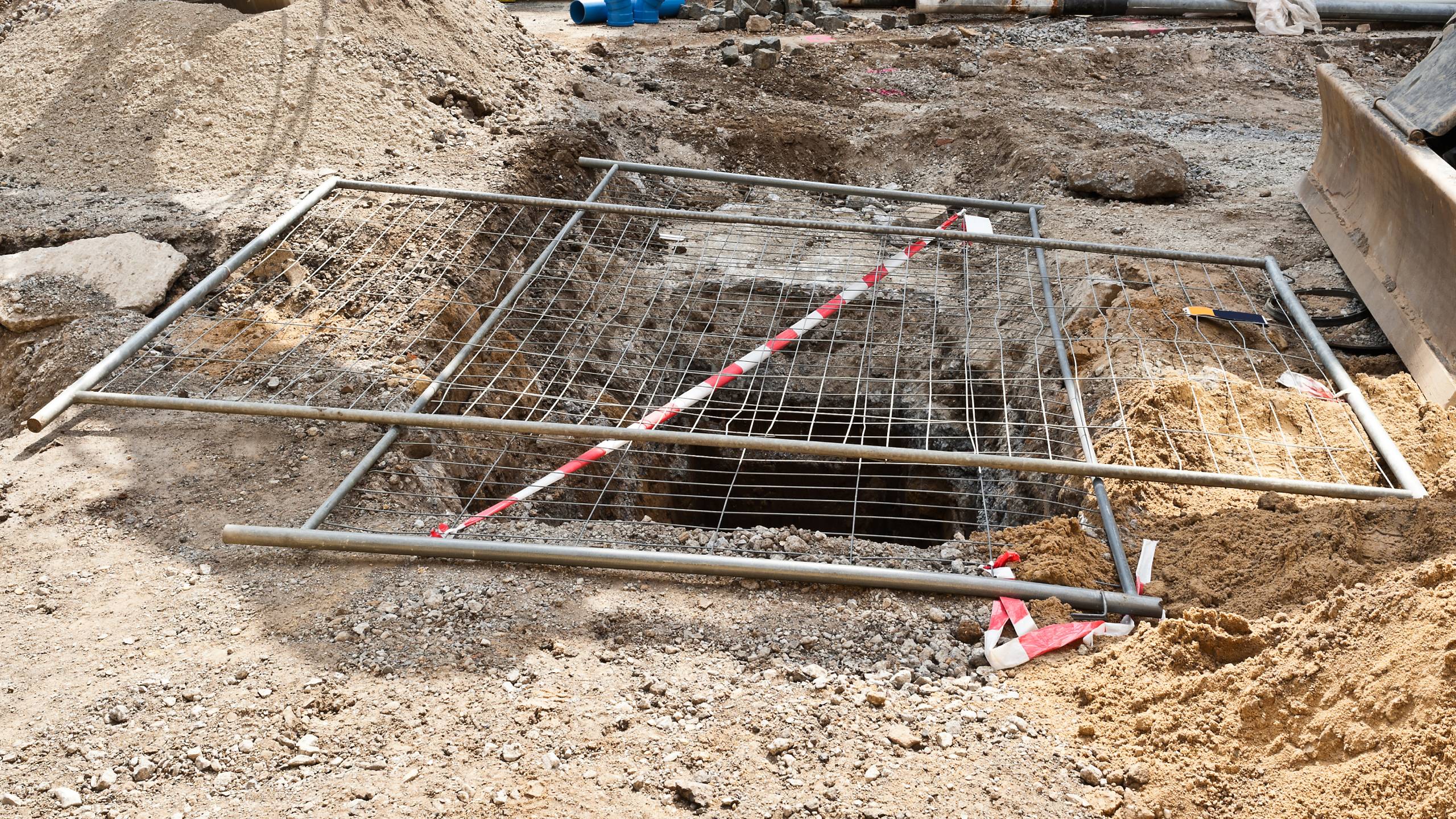 A deep hole in the ground on a building site is only provisionally covered with a construction fence.